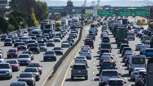 Heavy multi-lane traffic moves along a divided highway with green exit signs for Bay Area cities overhead